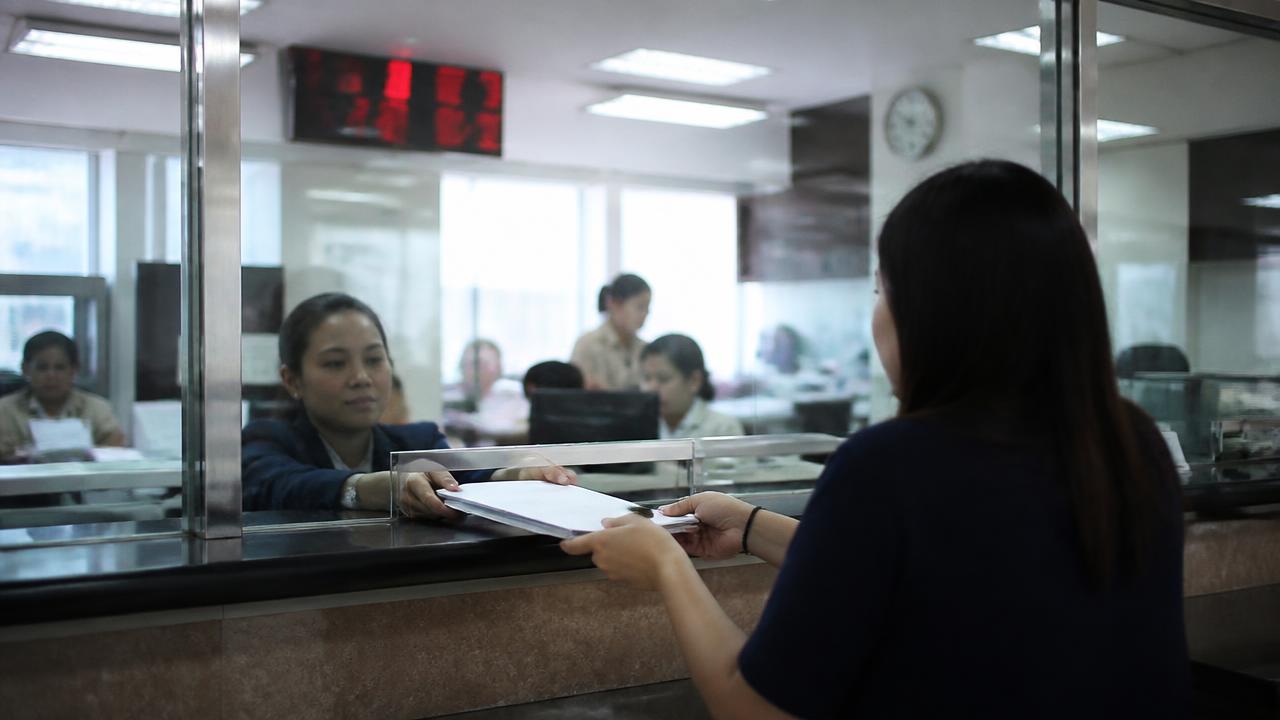 A consular service counter where an officer receives a document folder through a glass window